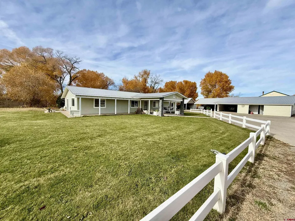A suburban house with a driveway and an adjacent garage, surrounded by green lawns and autumn trees.