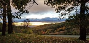 A scenic view of trees framing a colorful sunset over rolling hills.