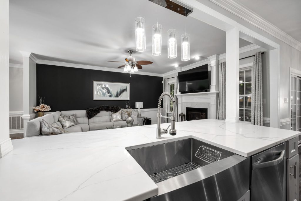 A modern kitchen with a white marble countertop and stainless steel sink, featuring stylish lighting and a black accent