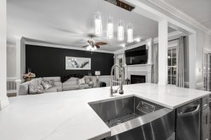 A modern kitchen with a white marble countertop and stainless steel sink, featuring stylish lighting and a black accent