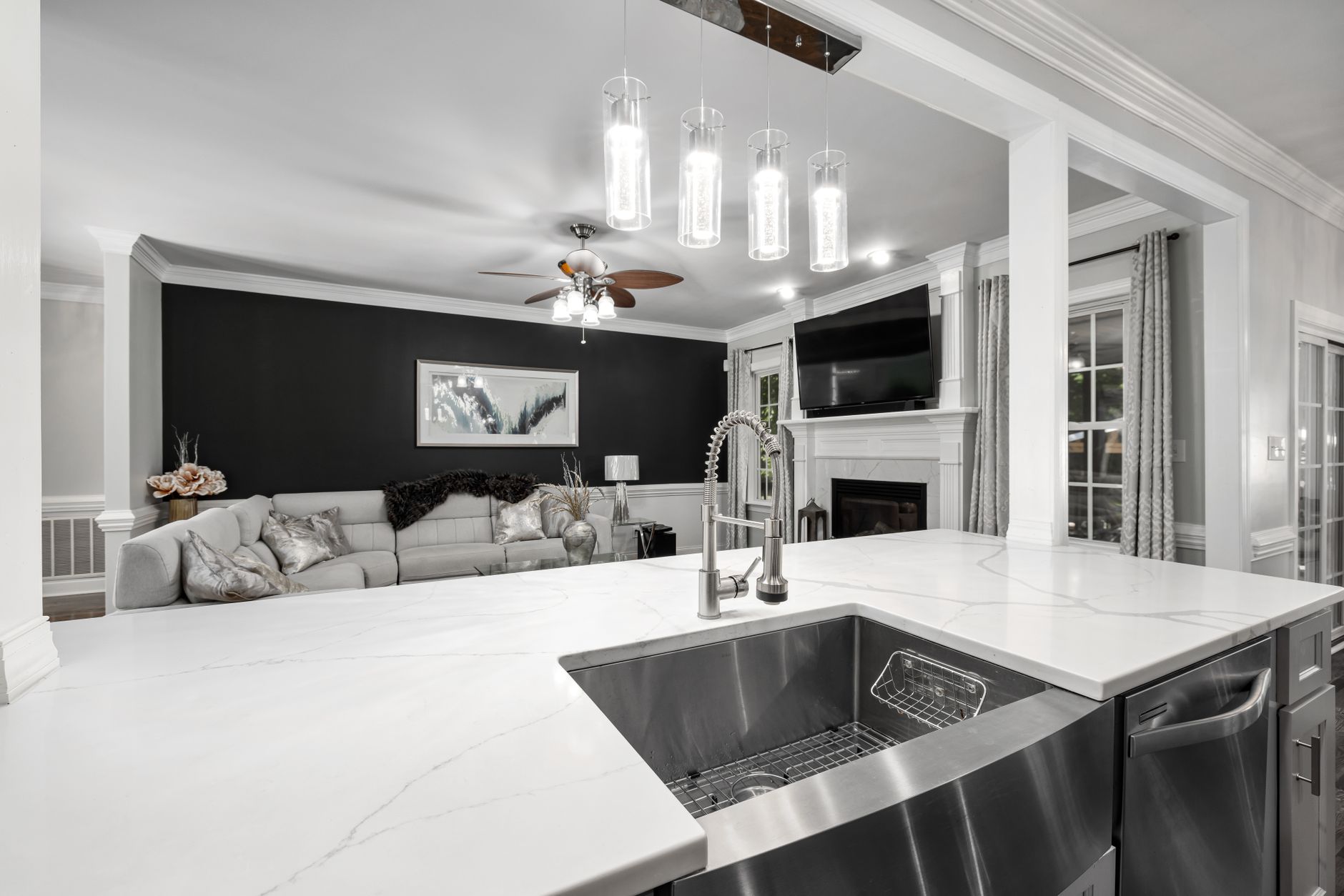 A modern kitchen with a white marble countertop and stainless steel sink, featuring stylish lighting and a black accent